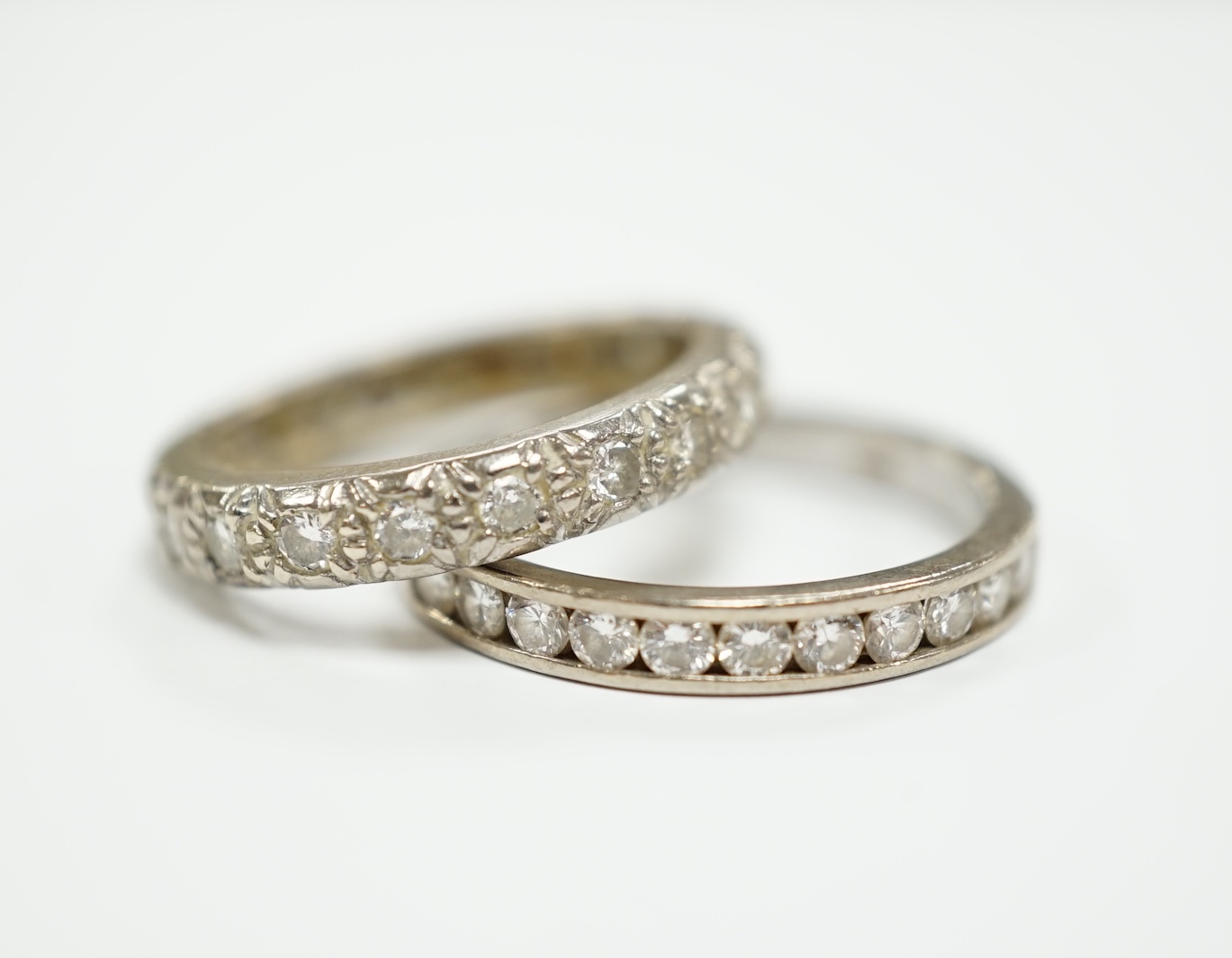 A white metal and diamond chip set full eternity ring, size L and a modern 18ct white gold and channel set diamond half eternity ring, size N/O.